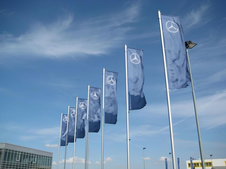 Blaue Flaggen mit dem Mercedeslogo wehen im Wind vor blauem Himmel im Hintergrund