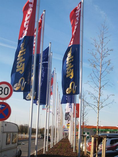 Mehrere Fahnenmäste mit Fahnen wehen auf einem Parkplatz im Wind