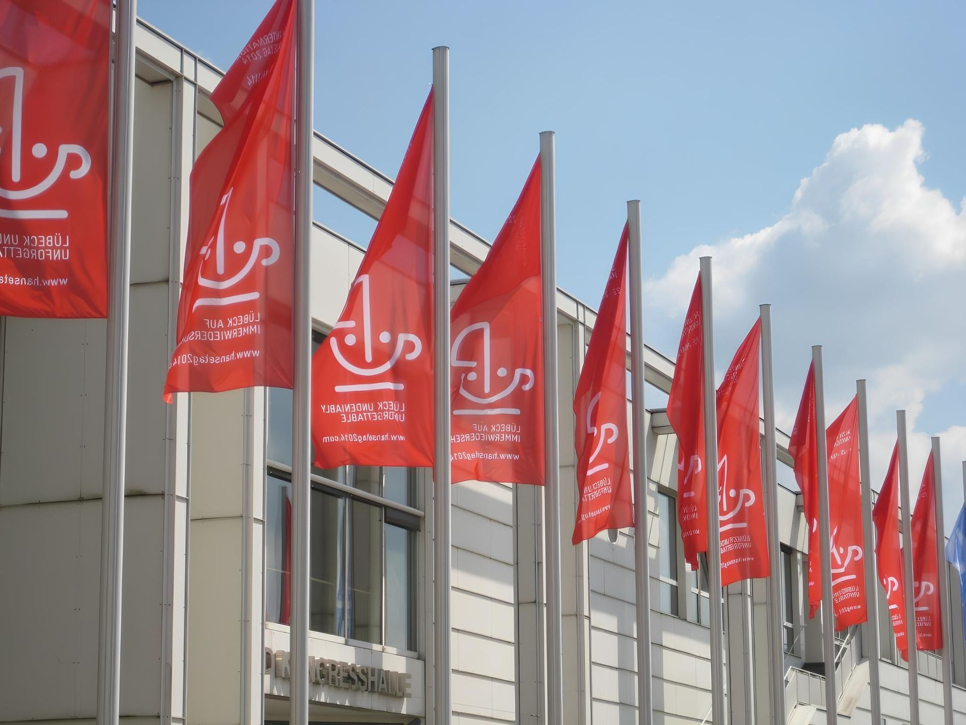 Rote Flaggen am Fahnenmast wehen im wind vor einem Gebäude im Hintergrund