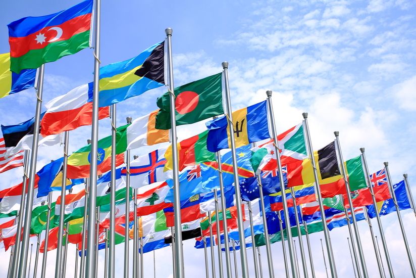 Mehrere Landesflaggen an Fahnenmästen wehen im Wind vor blauem Himmel