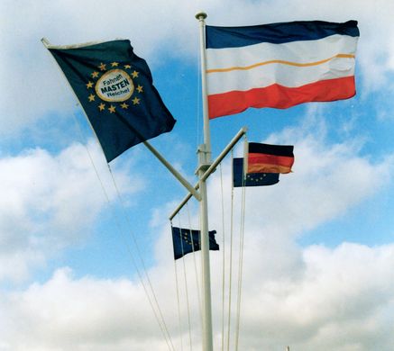 Ein Signalmast mit mehreren Fahnen vor blauem Himmel mit Wolken im Hintergrund