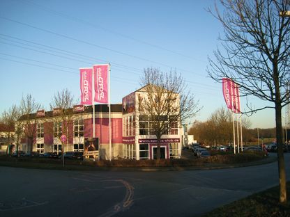Rote Fahnen wehen an einem Fahnenmast vor einem Gebäude im Wind vor blauem Himmel im Hintergrund